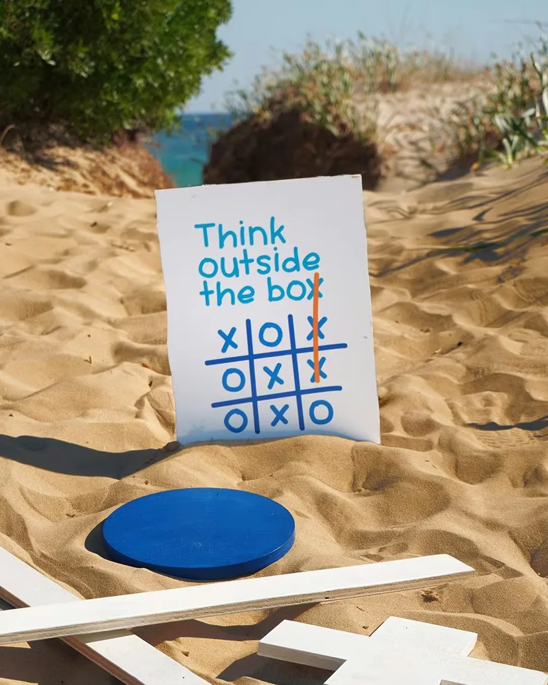 Cartello “Think outside the box” con lo schema del tris, piantato nella sabbia