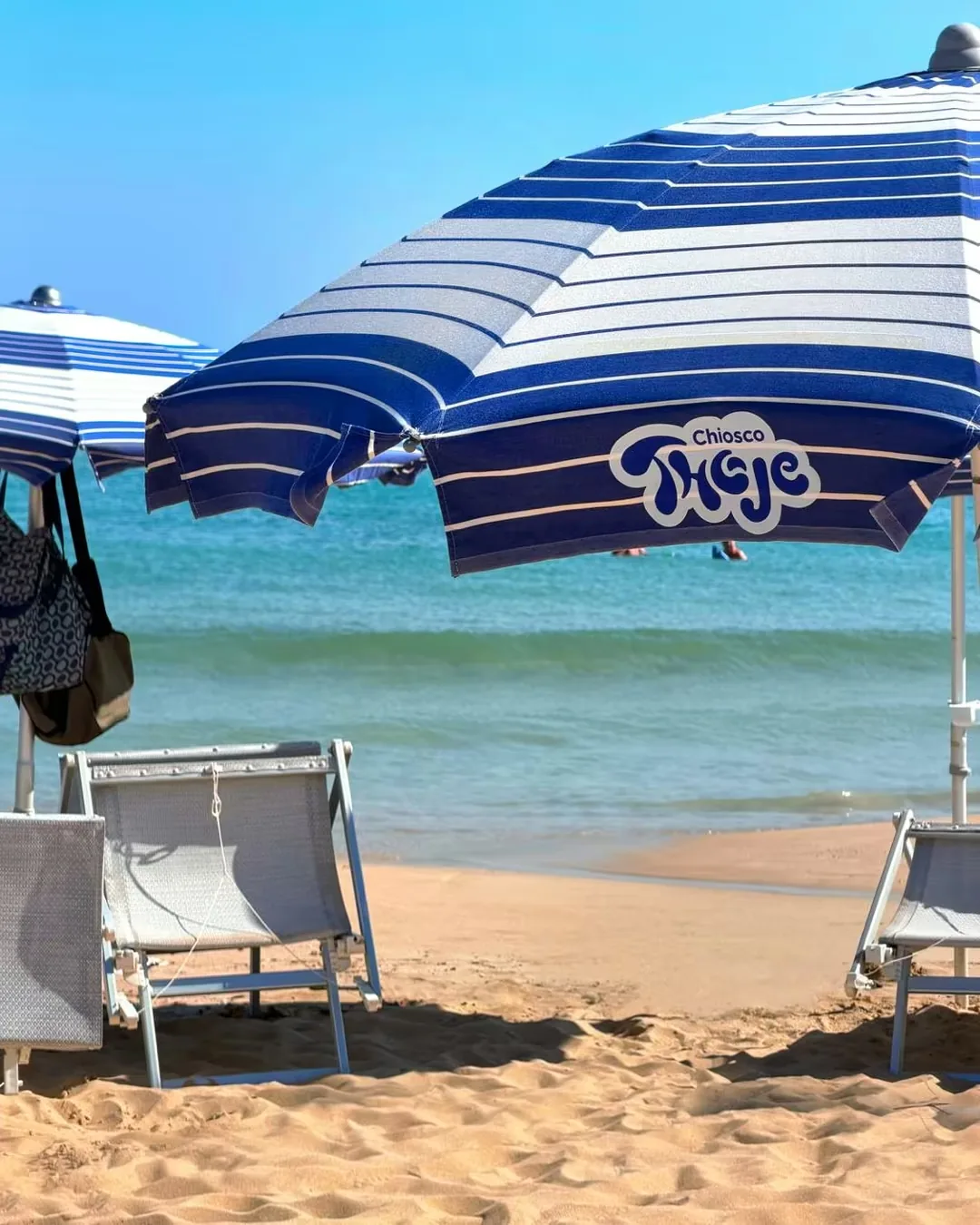 Ombrellone a righe blu con il logo Chiosco Thoje, davanti al mare di Pescoluse